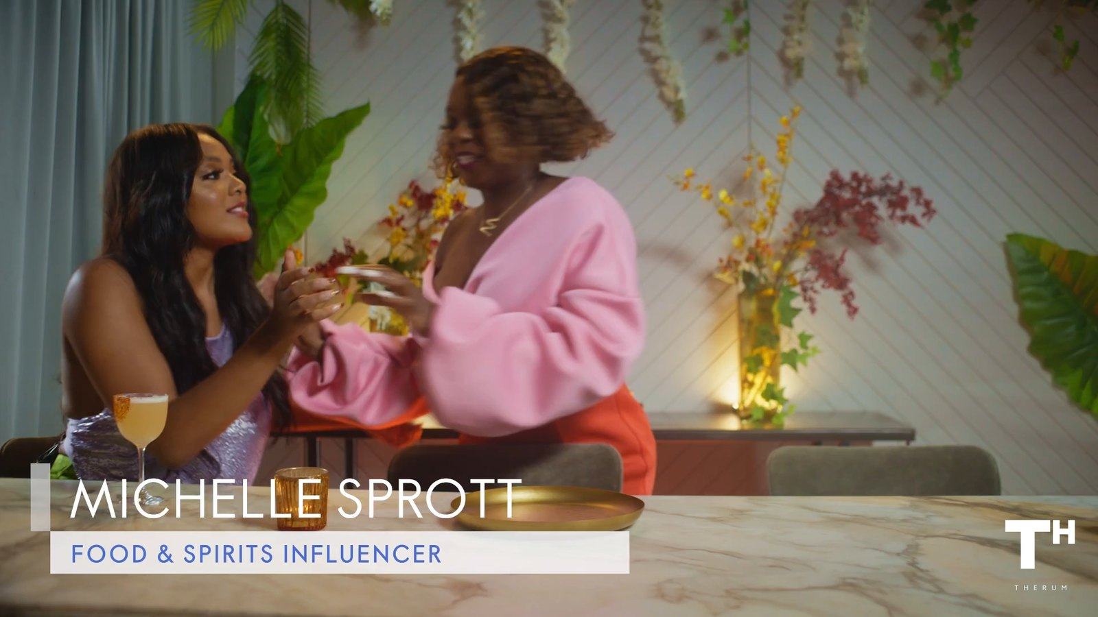Frame from the final video: Michelle Sprott’s lower third, Food & Spirits Influencer, at the table