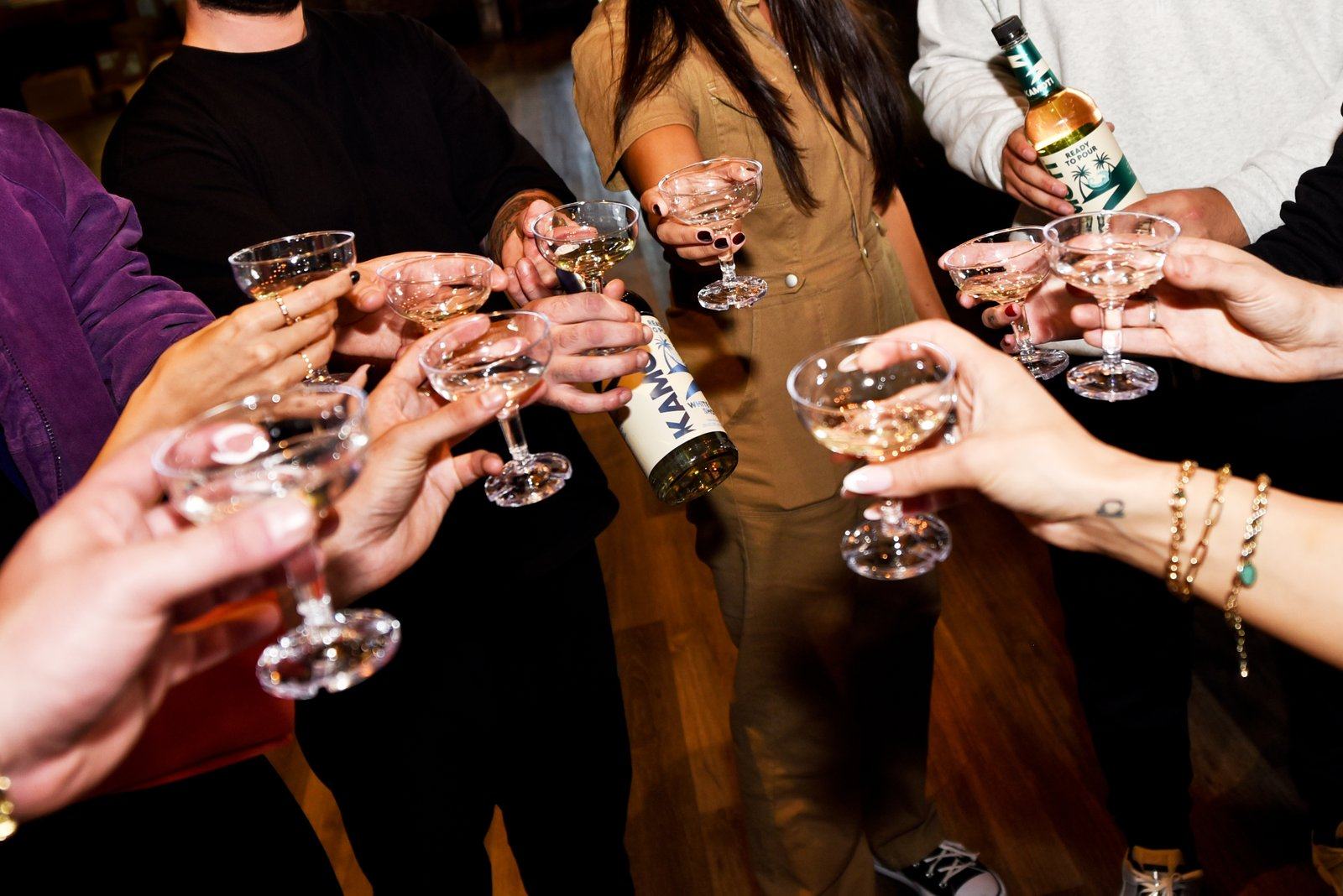 A group raising coupe glasses in a toast around a bottle of Kamoti