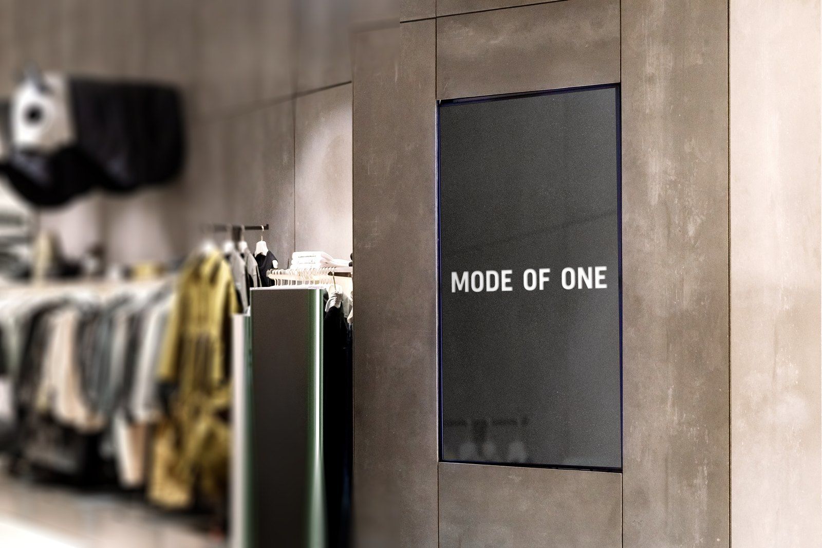 Store render: a Mode of One sign on a concrete column beside clothing racks