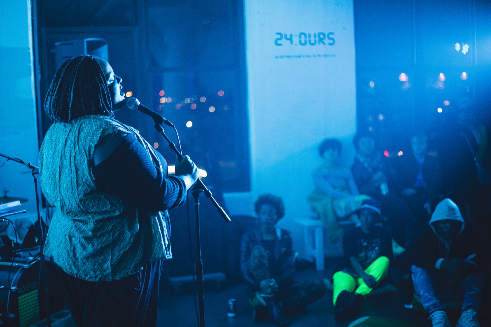 A performer with a flute on the 24:Ours stage under the wordmark