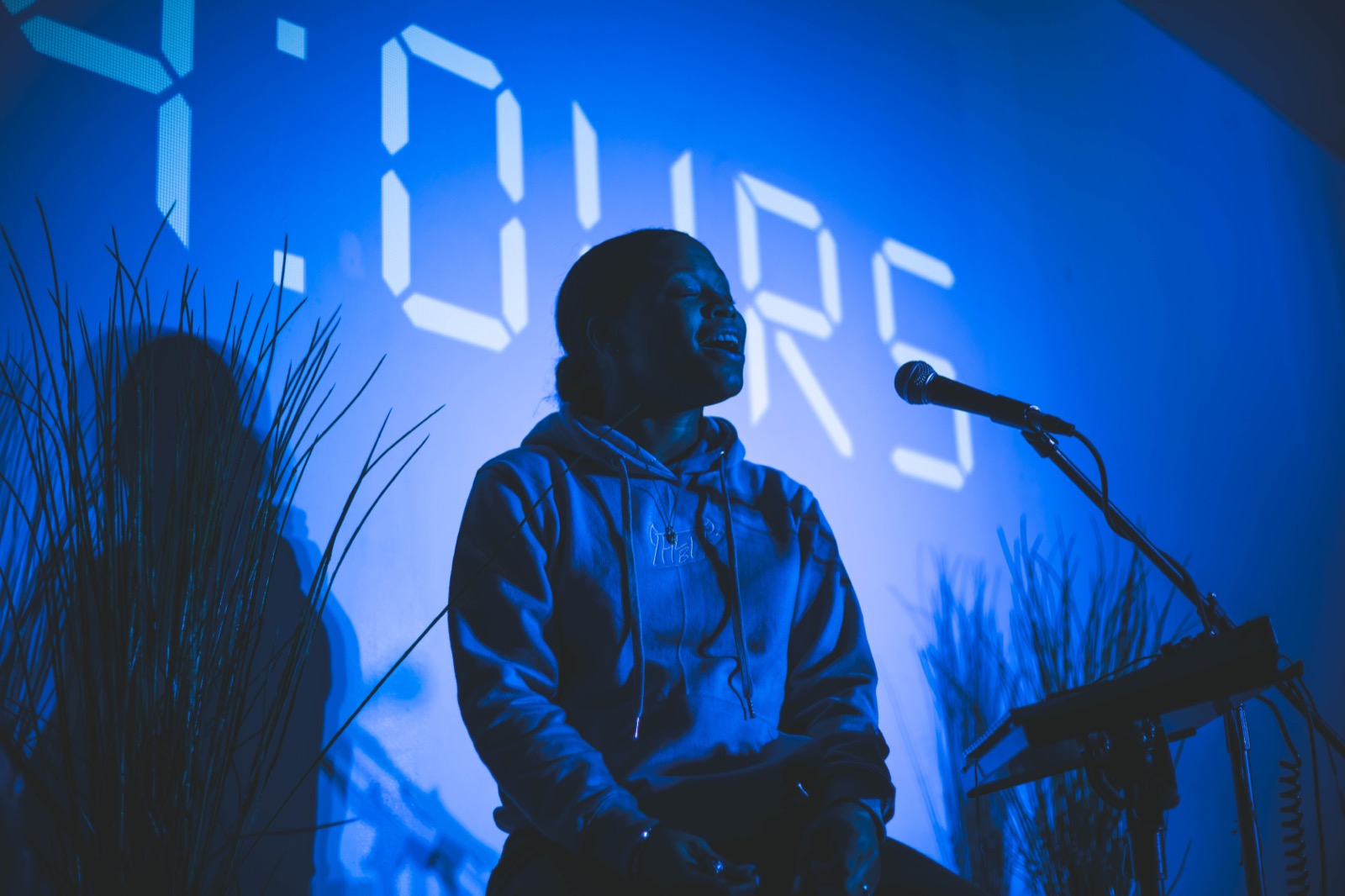 A singer at the microphone in front of the 24:Ours wordmark