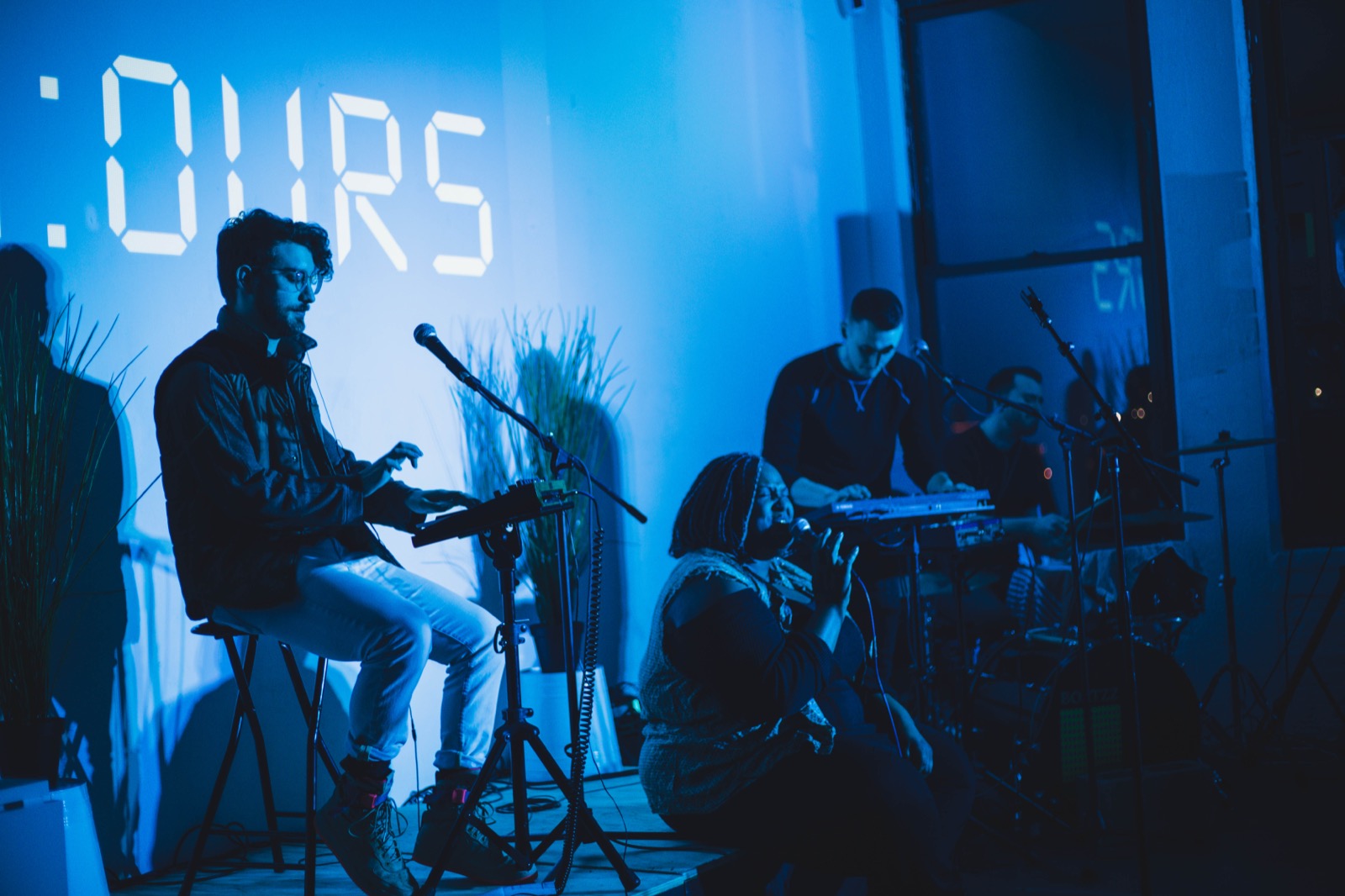 A guitarist performing in front of the 24:Ours digital clock wordmark