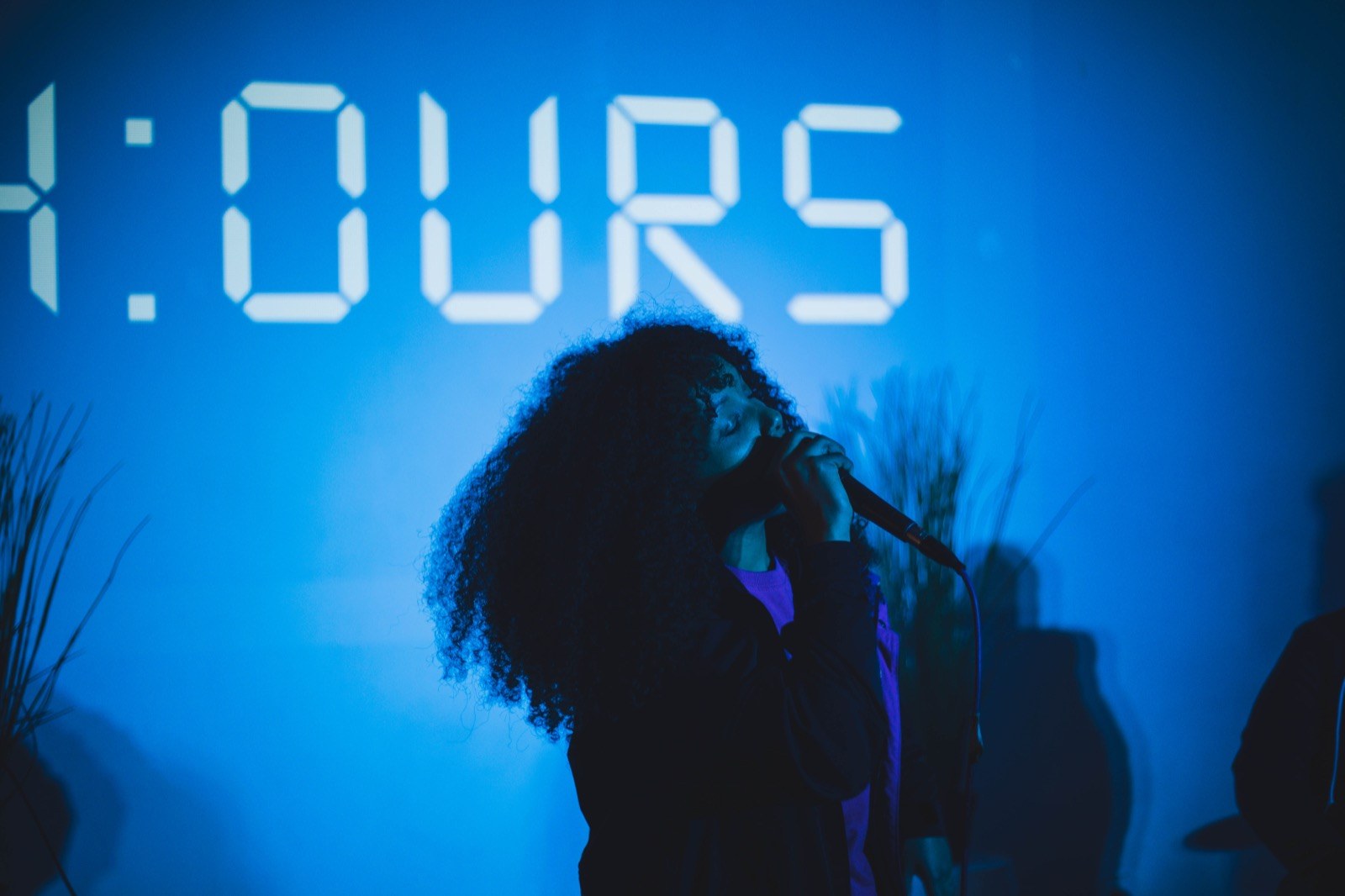 A singer in front of the 24:Ours wordmark during a set