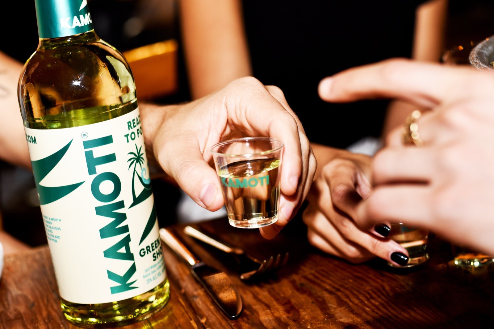 A Kamoti bottle and a shot raised in a crowd of hands