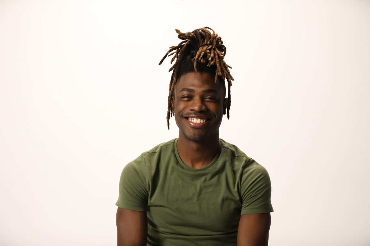 A smiling man with locs tied up, in a green t-shirt, from the LetsGetChecked photoshoot